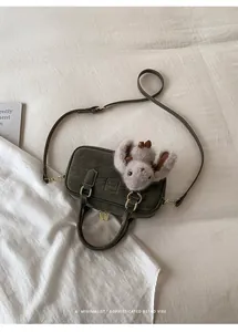 Detailed top view of dark grey-green leather pillow bag with plush bunny on white bedding