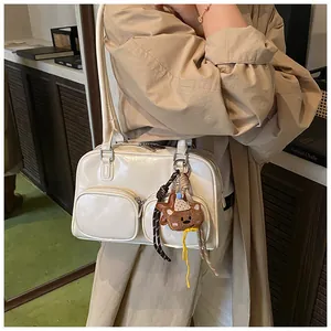 Dettaglio borsa a spalla in pelle color crema con ciondolo a forma di orsetto