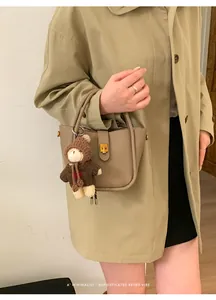 Detail der khakifarbenen Beuteltasche aus genarbtem Leder mit Teddybär-Anhänger und Schnalle