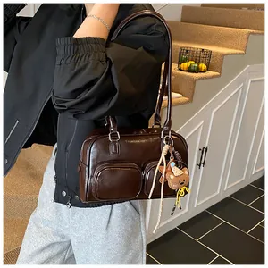 Dettaglio borsa in pelle lucida marrone scuro con doppie tasche e ciondolo a forma di orso