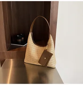 Detail of woven straw shoulder bag featuring brown leather trim and small charm card pouch