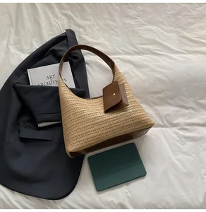 Detail of hobo straw bag with brown leather trim and mini pouch on white fabric