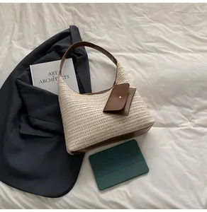 Detailed view of woven straw tote bag with brown leather trim and hanging mini pouch