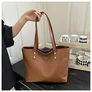 Detail of brown woven tote bag showing fine texture, slim handles and silver rivet accents
