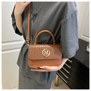 Détail d'un sac à main marron tressé avec boucle dorée en M et finitions en cuir
