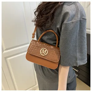 Détail d'un sac à bandoulière marron avec boucle dorée M, porté par un mannequin