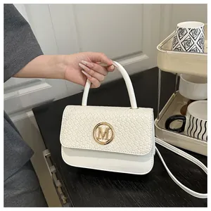 Détail du sac à main blanc tissé avec boucle dorée en M tenu à la main dans un intérieur