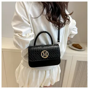 Détail du sac tressé noir avec logo M doré et bandoulière dans un décor élégant