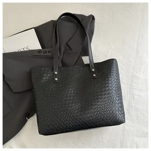 Detailed close-up of black woven tote bag with silver hardware on grey blazer background
