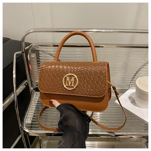 Détail d'un sac à main marron avec rabat en cuir tressé et boucle dorée logo M
