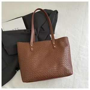 Close-up of brown woven tote bag showing leather texture and silver rivet reinforcement