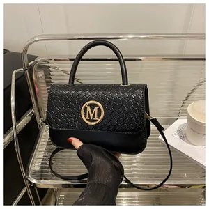 Détail du sac à main noir en similicuir avec rabat tressé et logo doré métallique