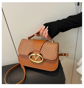 Detail of caramel brown leather handbag with woven flap and oval V-shaped metal lock