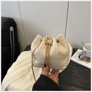 Détail du sac seau tissé crème avec chaîne dorée et élégante breloque en perle