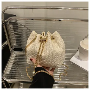 Détail du sac seau en paille avec chaîne dorée et fermeture à cordon coulissant