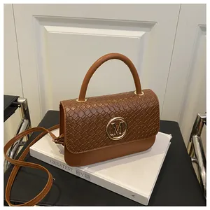 Détail du rabat tressé et du logo M doré sur un sac à main en cuir marron