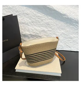 Detailed close-up of woven straw bucket bag with dark stripes and leather strap