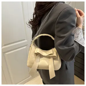 Détail d'un sac à main blanc crème avec nœud décoratif et bandoulière en chaîne argentée