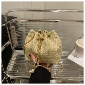 Détail d'un sac seau en paille avec chaîne dorée et élégants cordons ornés de perles