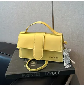 Detail of yellow faux leather shoulder bag with FASHION text and pearl ribbon charm