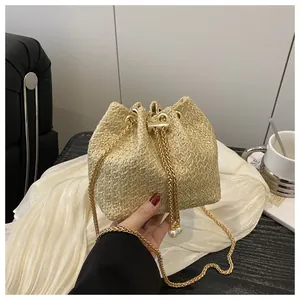 Détail du sac seau en paille avec chaîne dorée et cordon orné de perles élégantes