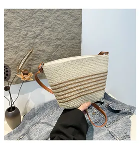 Close-up of woven straw bucket bag with dark brown stripes and smooth leather strap