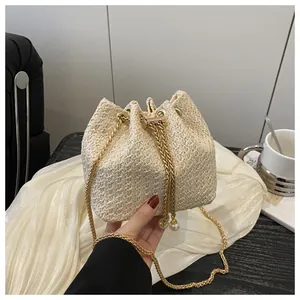 Détail du sac seau en paille tissée beige avec chaîne dorée et accents de perles