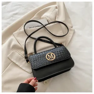 Détail du sac noir avec logo M doré posé sur un blazer beige avec carte élégante