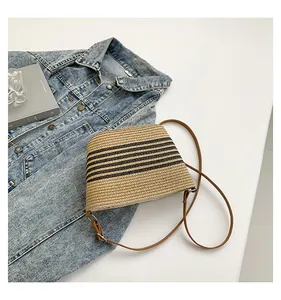 Close-up of a striped straw bucket bag with brown leather strap over denim background