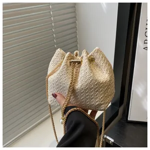 Détail du sac seau en paille avec chaîne dorée et perle décorative élégante