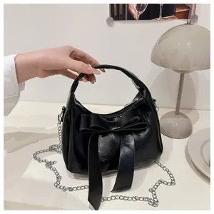 Détail d'un sac en cuir PU noir avec un grand nœud décoratif et une bandoulière chaîne