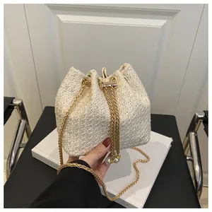 Détail du sac seau en paille crème avec chaîne dorée et cordon de serrage à perles