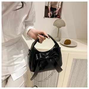 Détail d'un sac à main noir brillant avec un grand nœud et une bandoulière chaînette