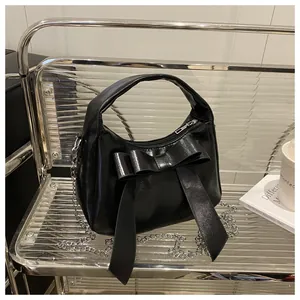 Détail du sac à main noir brillant avec un grand nœud décoratif et une chaîne argentée