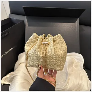 Détail du sac seau en paille avec chaîne dorée, pendentif perle et fermeture à cordon