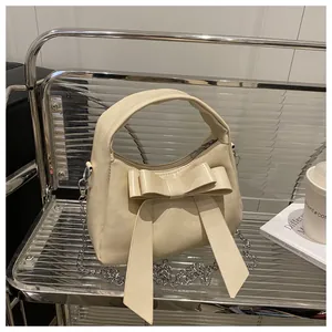 Détail d'un sac à main blanc cassé avec un grand nœud et une bandoulière chaîne