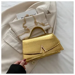 Detail of glossy gold crocodile pattern handbag with V-shaped buckle on beige blazer