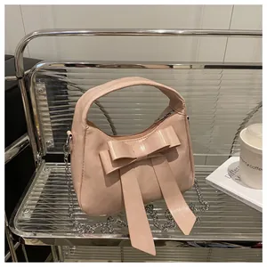 Détail du sac à main rose clair avec un grand nœud décoratif et une bandoulière en chaîne
