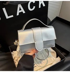 Close-up of metallic silver handbag featuring a fashion logo and pearl handle chain detail