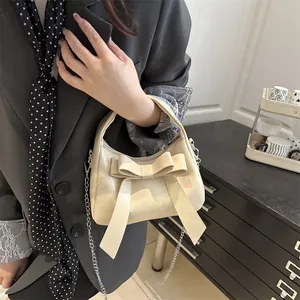 Sac à main beige chic avec nœud et bandoulière en chaîne dans un décor élégant
