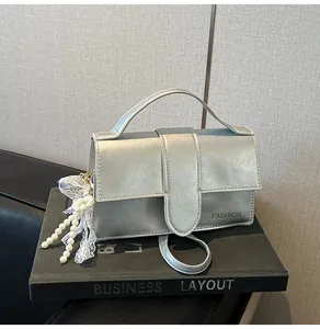 Detail of silver metallic handbag with pearl lace charm and fashion logo on book