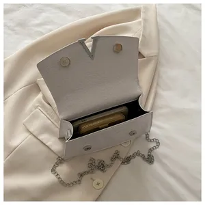 Close-up of white crocodile pattern handbag featuring a V-shaped silver buckle and chain