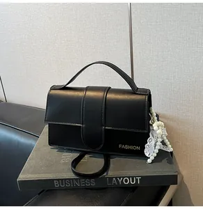 Close-up of black leather handbag with gold lettering, pearl charm, and lace detail
