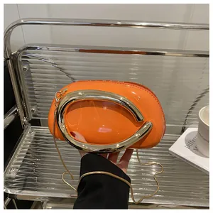 Détail du sac en cuir verni orange vif avec poignée métallique dorée en forme de U