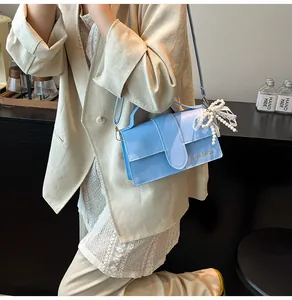 Detail of light blue glossy shoulder bag with gold logo and pearl bow lace charm accessory