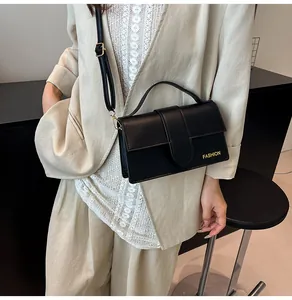 Detail of minimalist black leather crossbody bag with gold Fashion lettering worn with suit