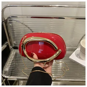 Détail de la pochette rouge vernie avec poignée dorée et fine bandoulière en chaîne