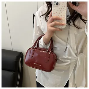 Détail d'un sac à main bordeaux en cuir brillant avec texte et finitions argentées