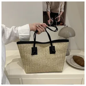 Detail of straw woven tote bag with black leather handles and elegant knot decoration