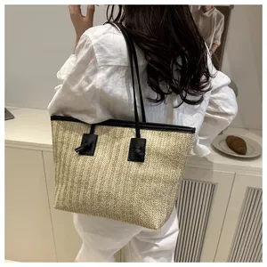 Detail of herringbone straw tote bag with black leather straps on white outfit